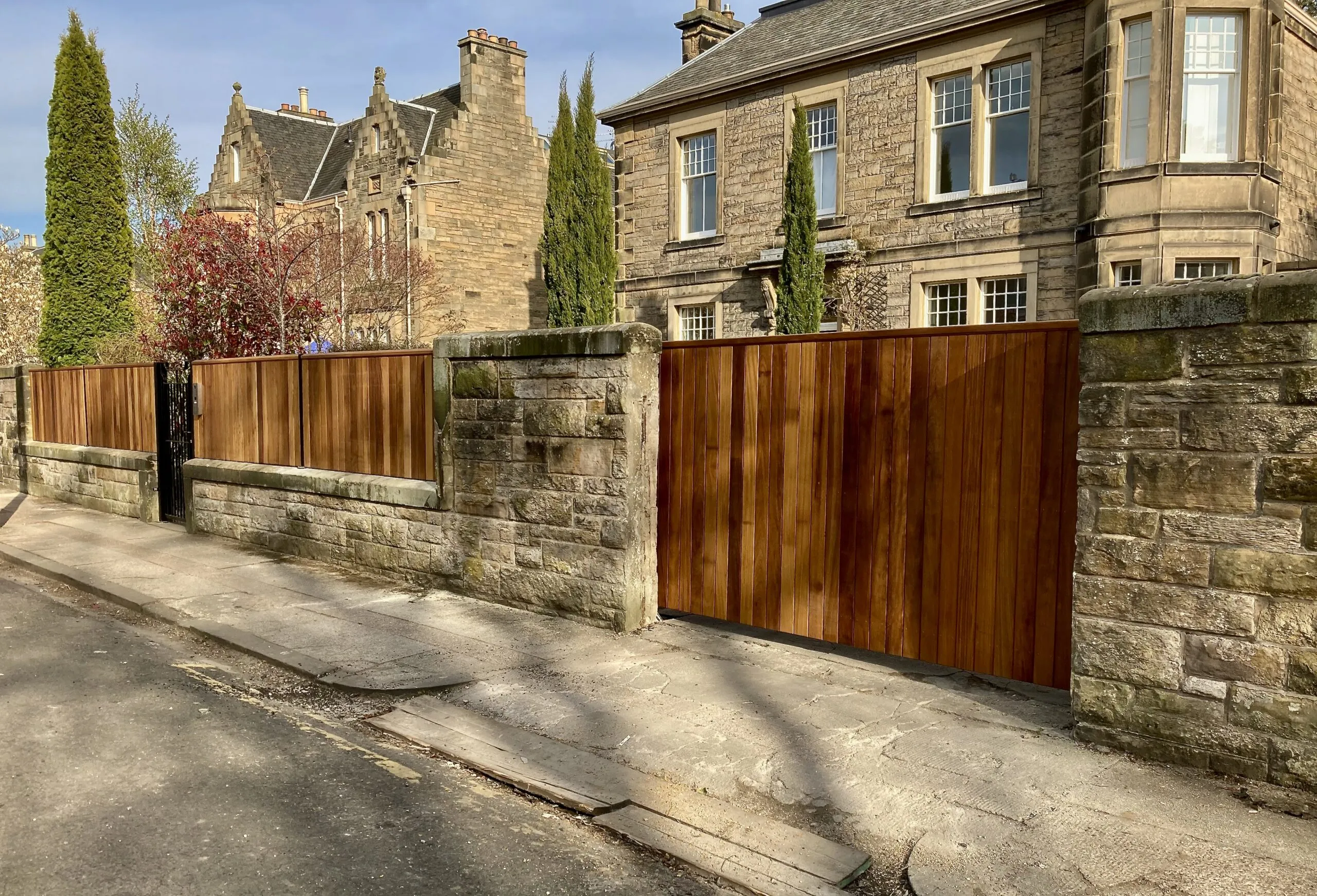 Solid iroko hardwood cantilever sliding gate with matching wall top fencing panels installed in Edinburgh                      