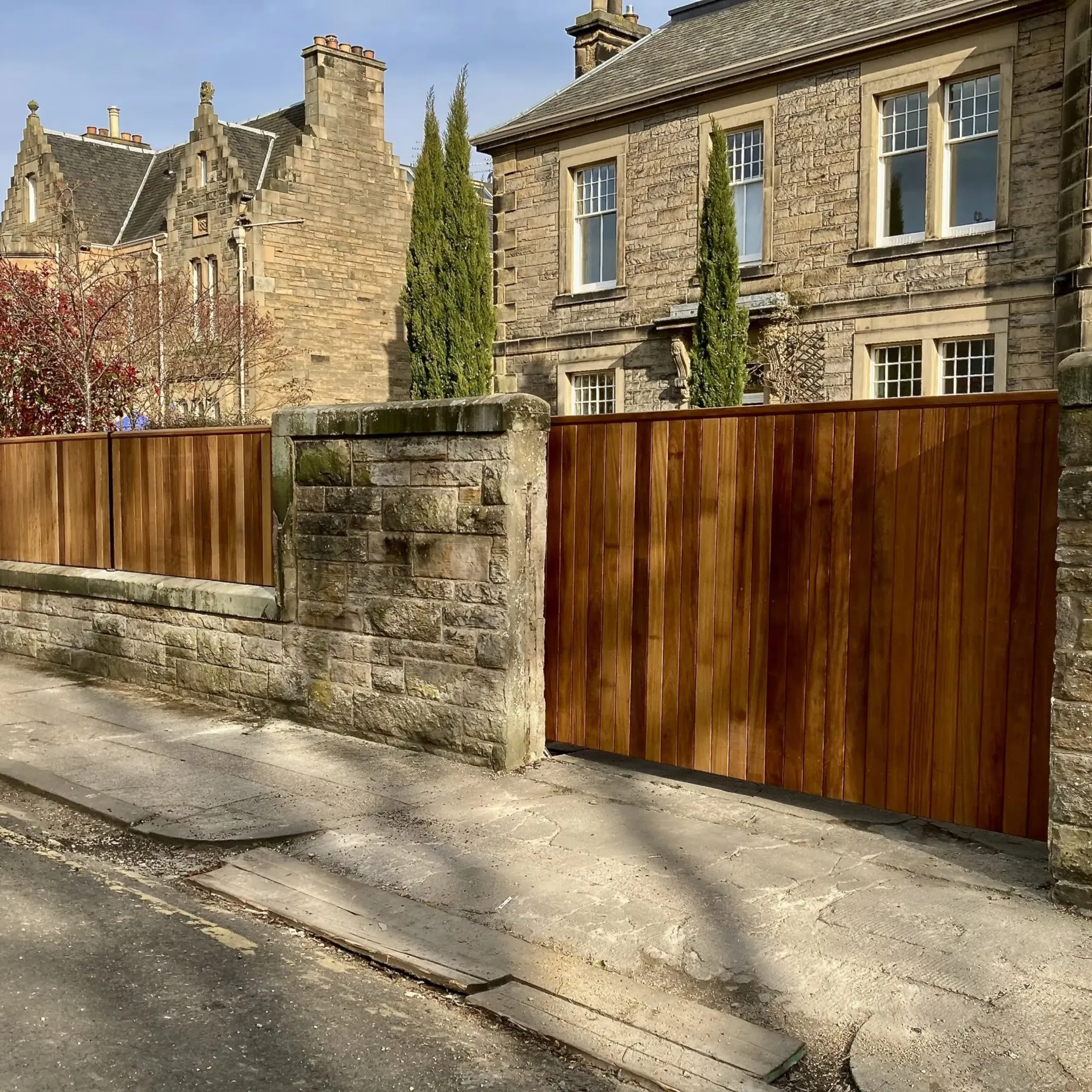 Solid iroko hardwood cantilever sliding gate with matching wall top fencing panels installed in Edinburgh                      